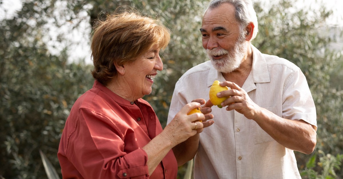 Elderly man and woman smiling and enjoying fruit.