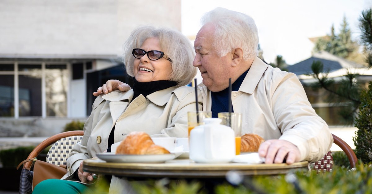 Elderly couple smiling and enjoying coffee outside.